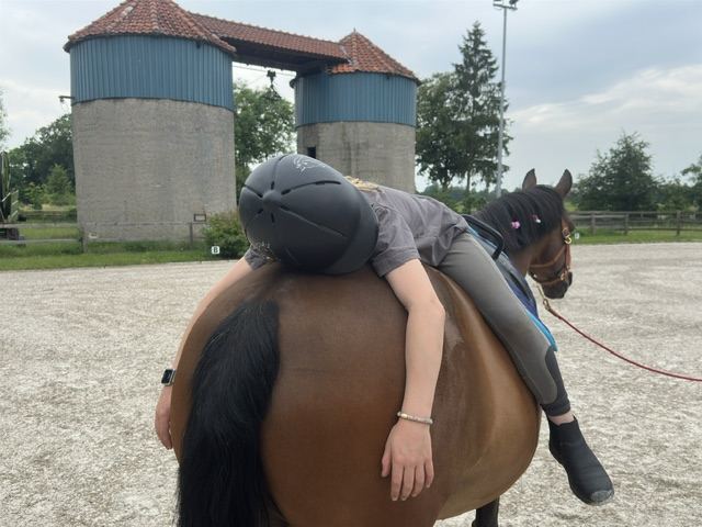 Ein Kind liegt bei der Reitergymnastik rücklings auf dem Pony