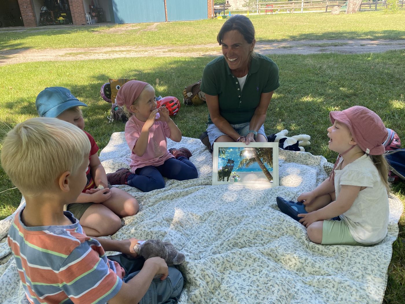 Kleine Kinder sitzen mit der Reitpädagogin auf einer Decke auf der Wiese