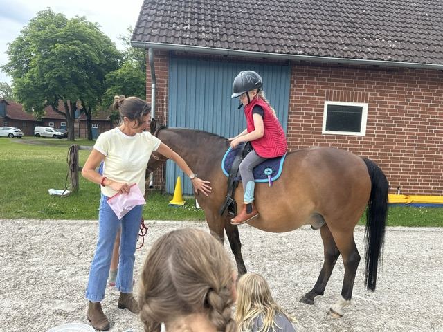 Ein Kind sitzt auf dem Pony vor dem Stall, die Reitpädagogin steht daneben
